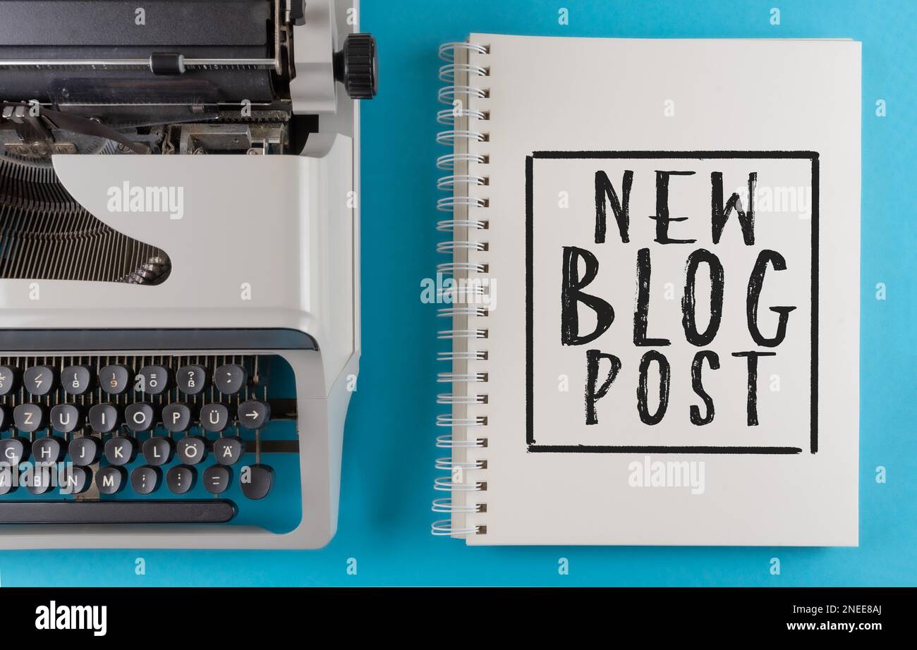 Text NEUER BLOG-BEITRAG auf Spiral-Notizblock auf farbenfrohem Schreibtisch mit alter Schreibmaschine, Inhaltserstellung und Blogging Konzept Stockfoto