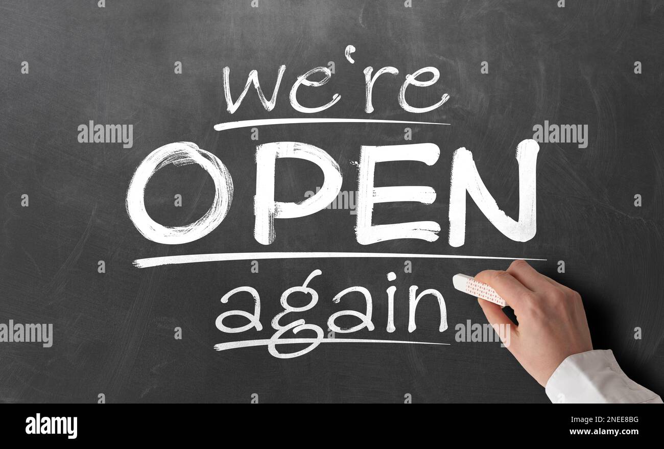 Person, die Text SCHREIBT, WIR SIND WIEDER auf der Tafel geöffnet, nach covid-19 Shutdown Konzept wieder geöffnet Stockfoto