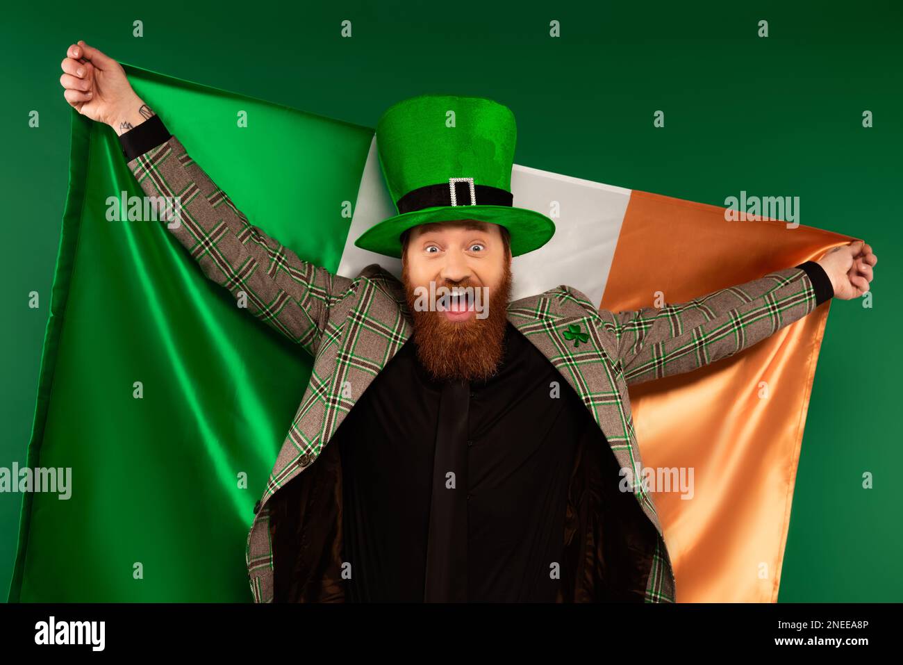 Aufgeregter bärtiger Mann mit Hut und irischer Flagge isoliert auf grünem Stock Image Stockfoto