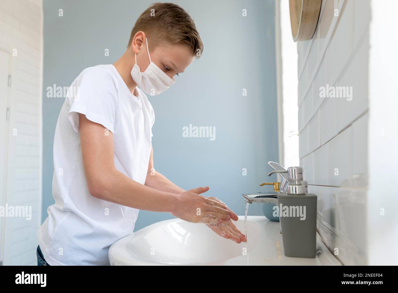Ein Junge, der eine medizinische Maske trägt und seine Hände wäscht, Seitenansicht. Hochauflösendes Foto Stockfoto