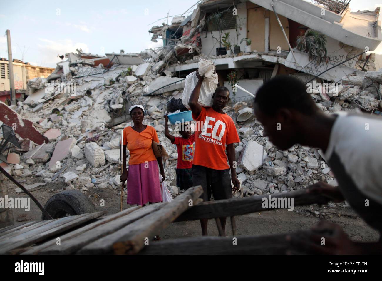 A family stands in front of a collapsed building as a man passes with ...