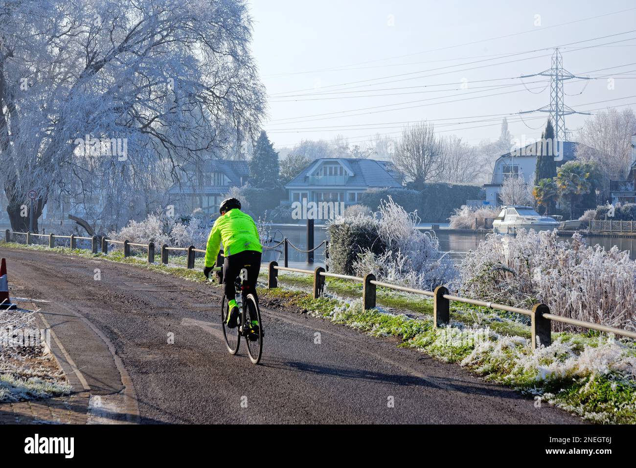 Ein einsamer Radfahrer auf dem Schleppweg in Shepperton an einem kalten, sonnigen Wintertag mit Bäumen und Vegetation bedeckt von Heiserfrost, Surrey England Stockfoto