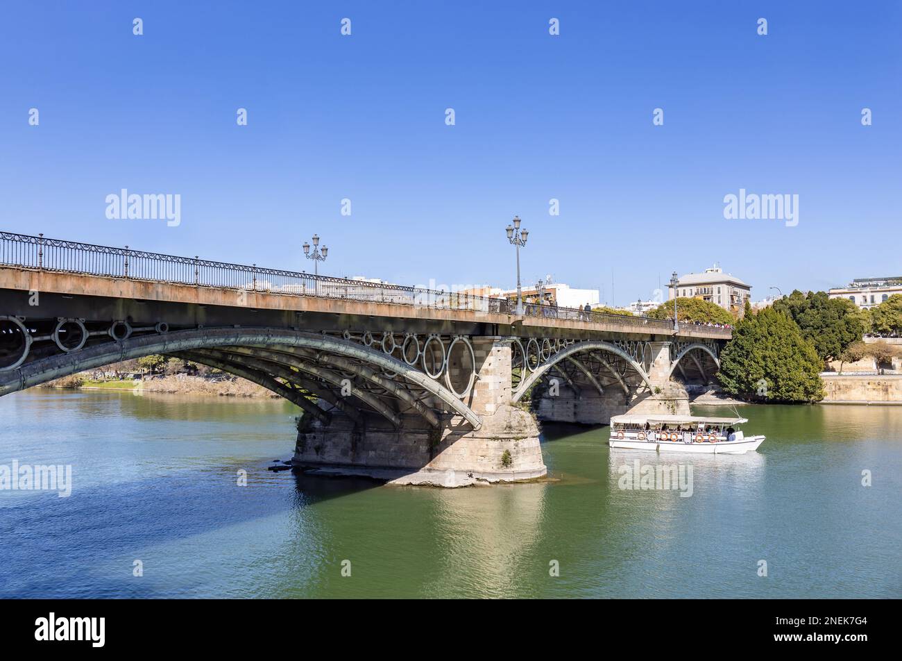 Die Überquerung des Touristenboots unter El Puente de Isabel II, auch bekannt als Puente de Triana, ist eine Brücke in Sevilla. Verbindet das Stadtzentrum mit dem Triana n Stockfoto