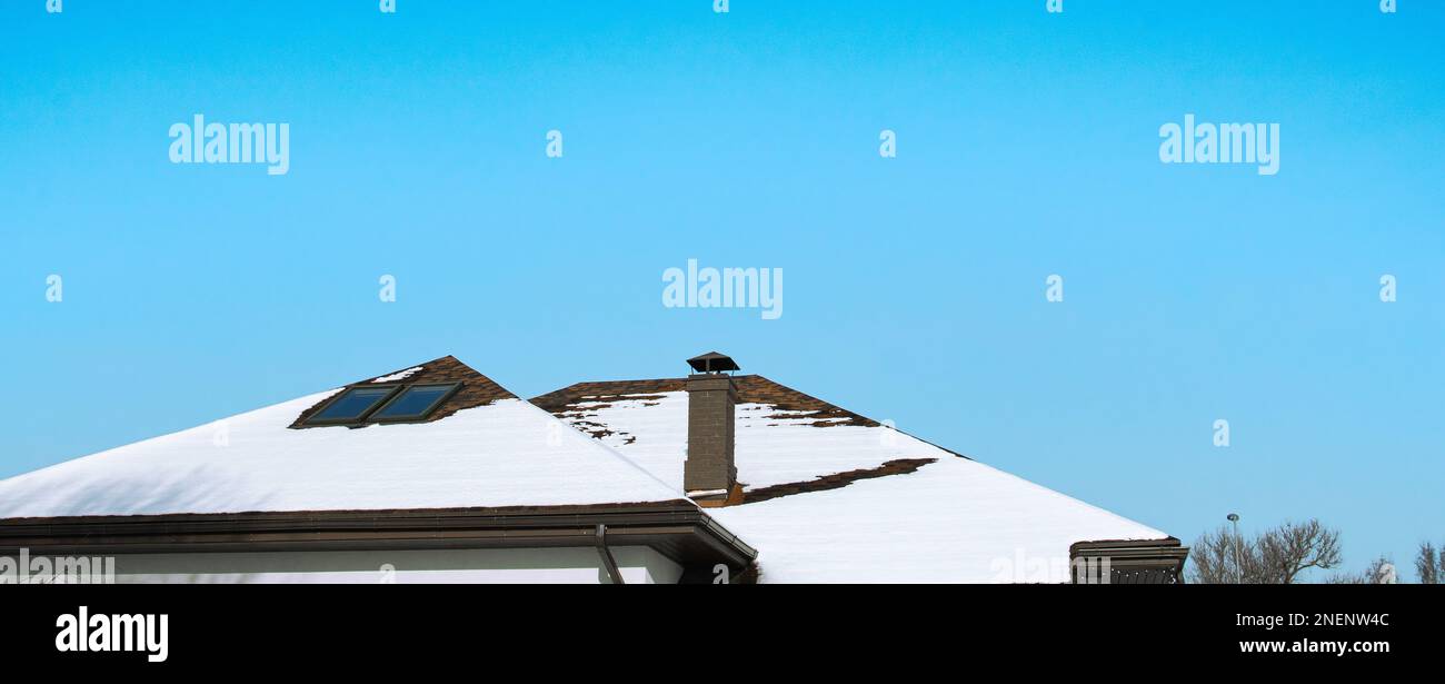 Schnee schmilzt auf dem Dach des Hauses unter den Strahlen der Februar Sonne, blauer Februar Himmel, der letzte Schnee verschwindet Stockfoto