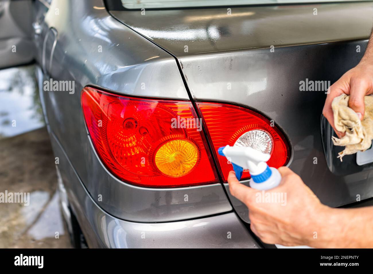 Mann wäscht Fahrzeug an der Selbstbedienungsstation der Autowaschanlage, sprüht Schaumreiniger aus der Sprühflasche auf die hinteren Kofferraumleuchten im Freien, reinigt Wischtücher Stockfoto