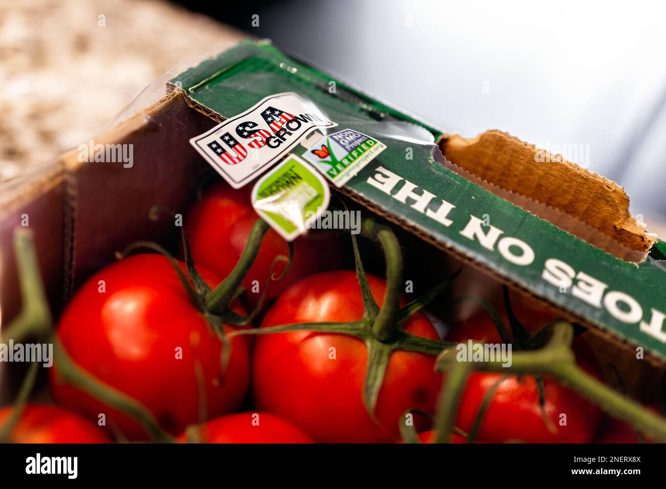 Avon, USA - 17. Juni 2022: Nahaufnahme von roten Tomatenfrüchten auf Weinreben in Karton mit Aufkleberetikett für „Grown in USA America“ mit Nongmo-Text und „Nobody“ Stockfoto