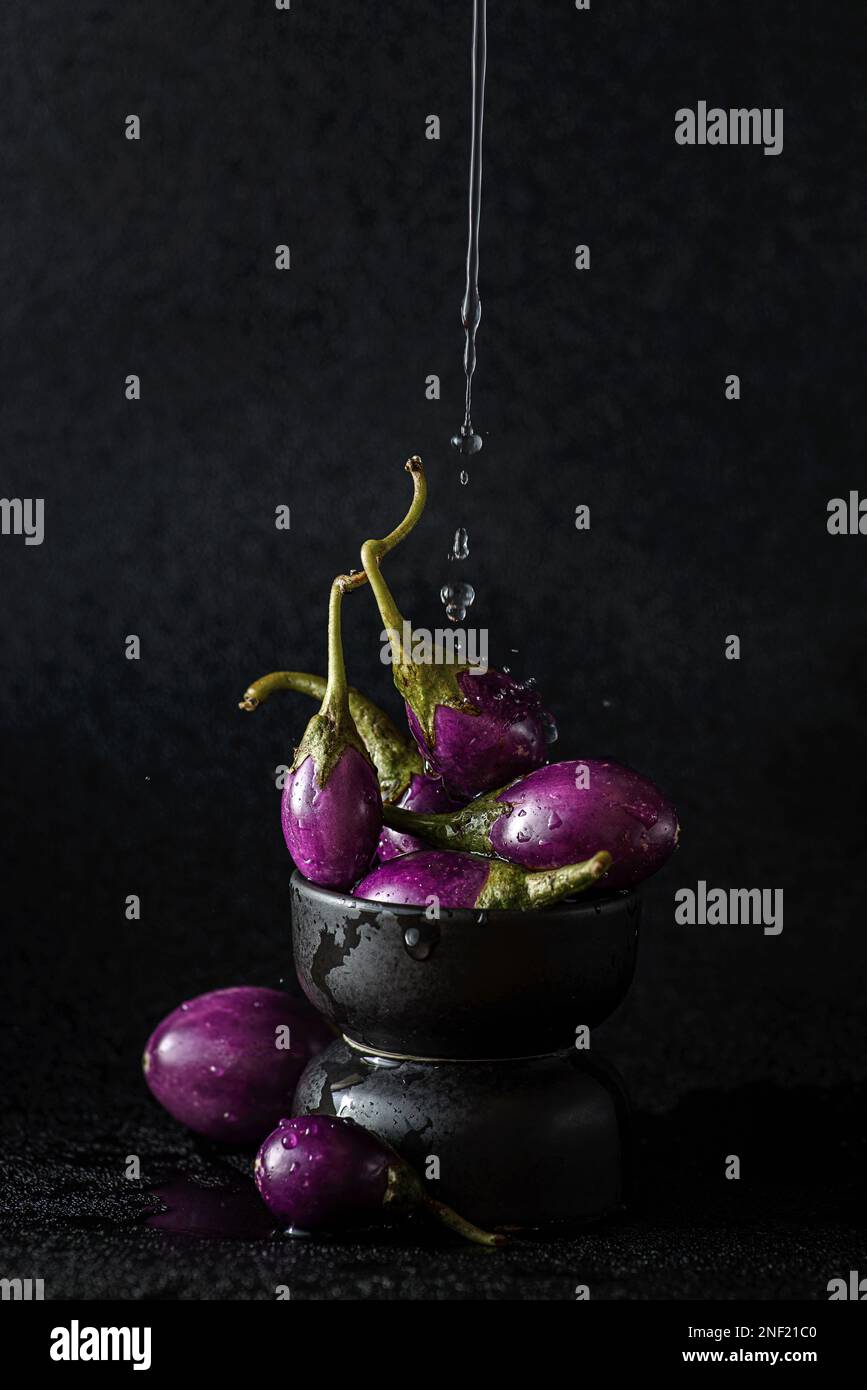 Kleine Aubergine auf schwarzem Hintergrund. Wasser gießt über die Aubergine, hochwertiges Foto Stockfoto