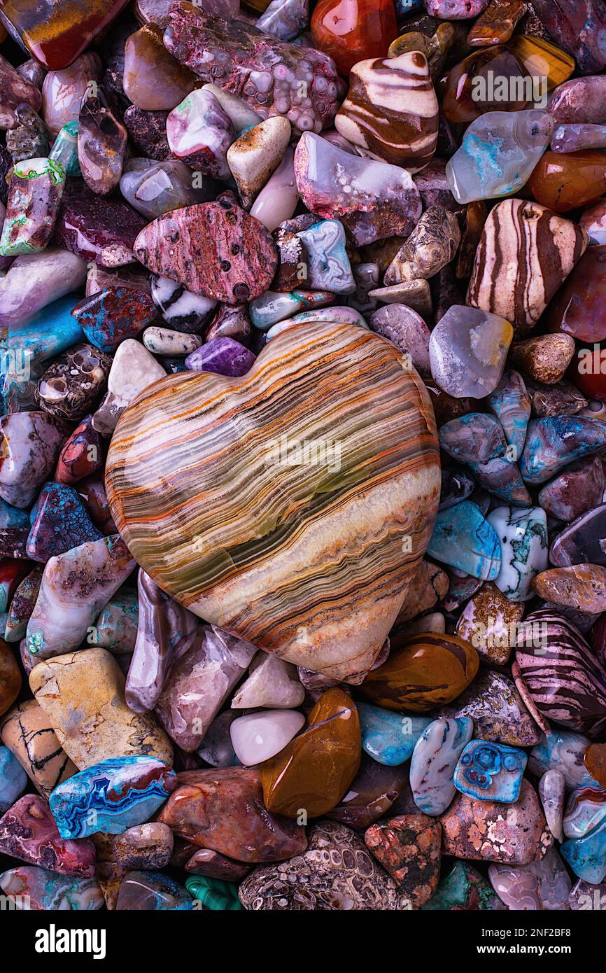 Herzförmiger Stein auf einem Haufen wunderschöner farbiger Steine und Felsen Stockfoto