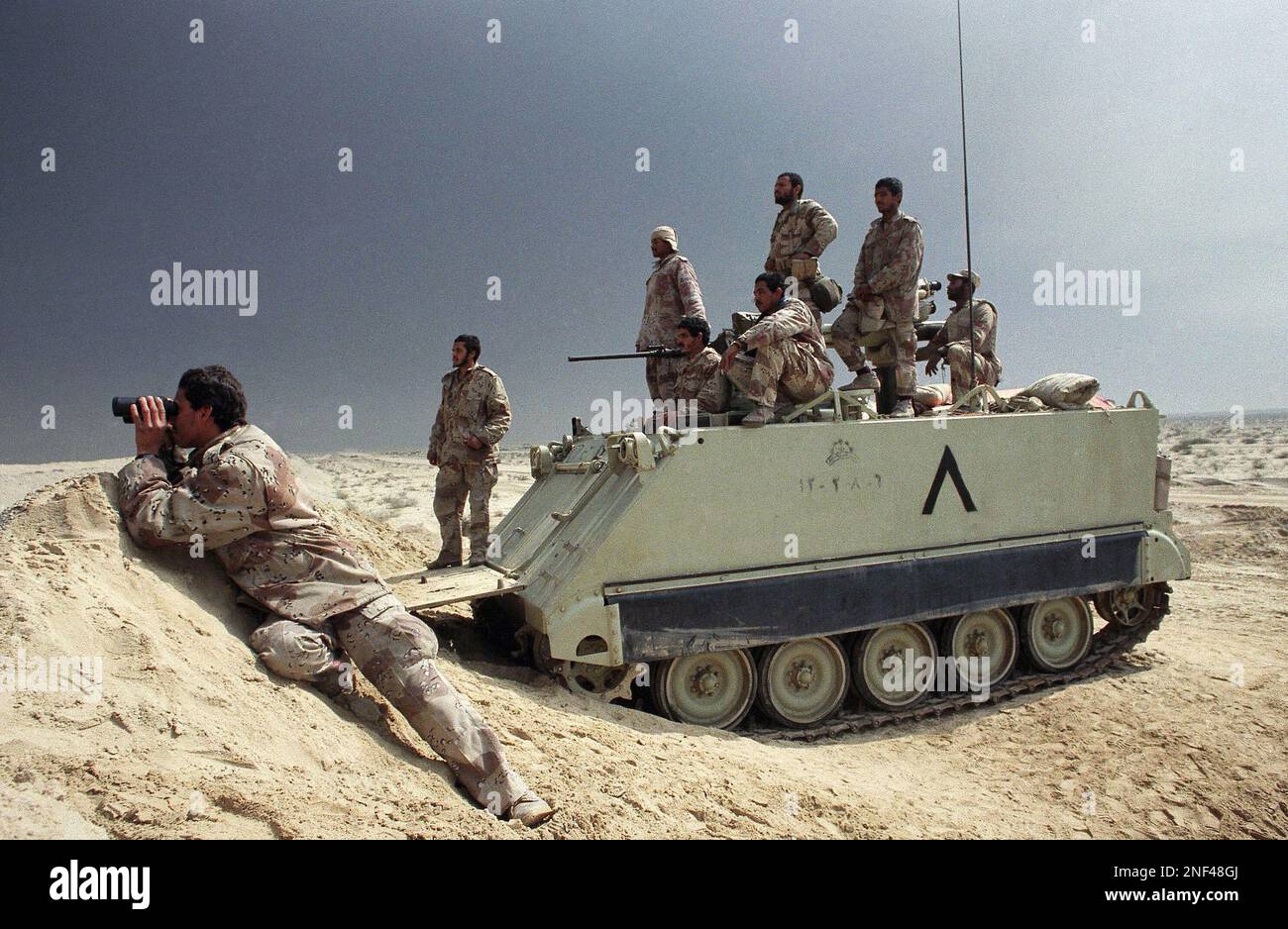 Saudi troops on an armored personnel carrier near the Kuwait border look toward suspected Iraqi positions, Saturday, Feb. 23, 1991 in Saudi Arabia as the waiting continued at the border. Smoke from burning oil wells in Kuwait darkens the midday sky. (AP Photo/Laurent Rebours) Stockfoto