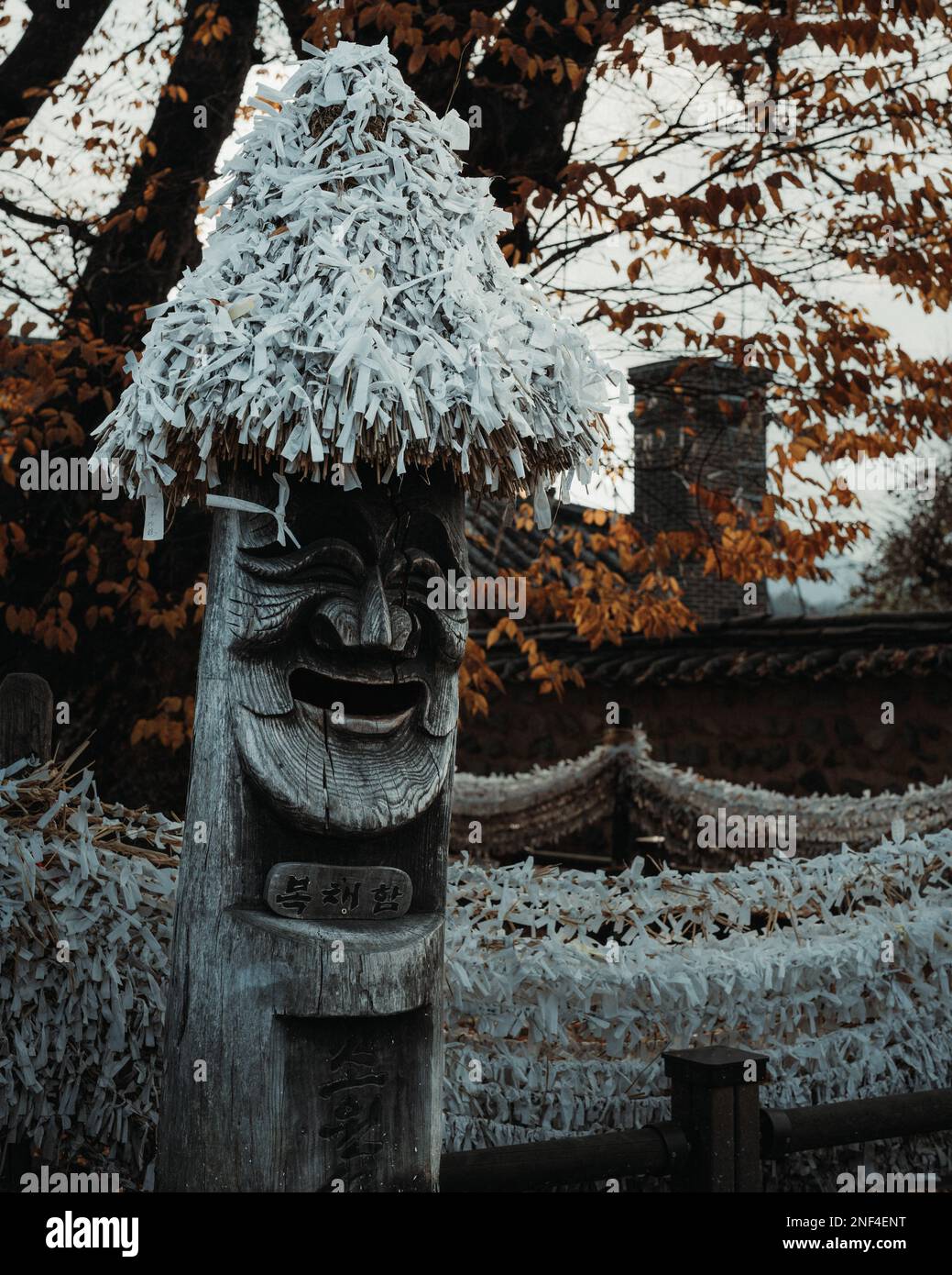 Jangseung, eine Art koreanischer Totempfahl, der vor einigen Herbstblättern im Hahoe Folk Village in Andong, Südkorea lächelt. Stockfoto
