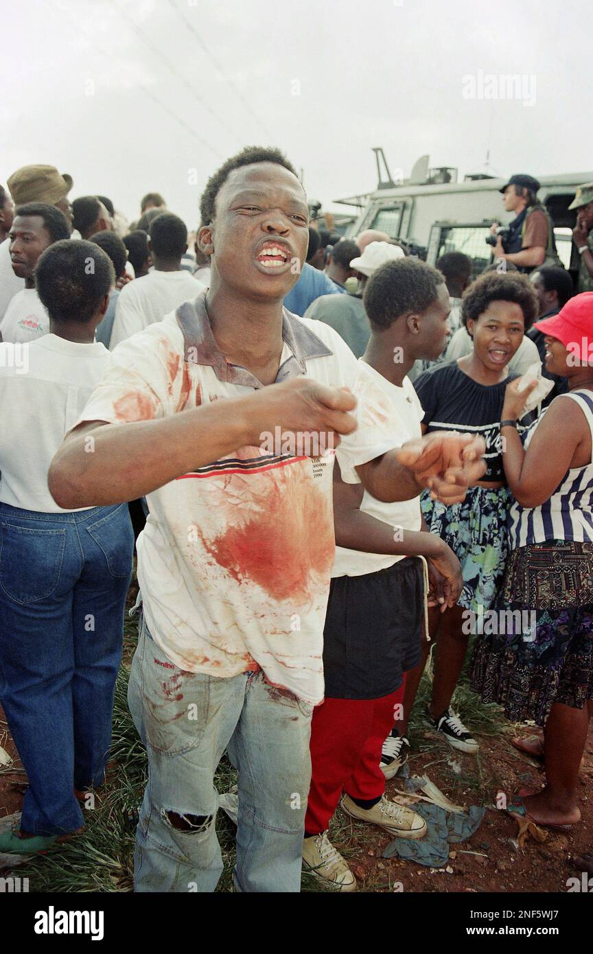 A Katlehong resident with blood over his clothes snarls at the press to leave on Sunday Jan. 9, 1994 in South Africa after an African National Congress convoy carrying ANC General Secretary Cyril Ramaphosa and South African communist Party leader Joe Slova, came under fire. A photographer for the Associated Press, Abdul Shariff was killed in the attack and two other journalists were wounded. (AP Photo/David Brauchli) Stockfoto