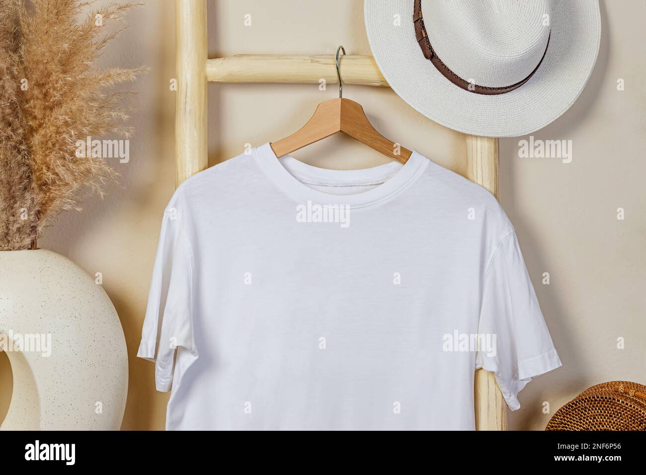 Weißes Baumwoll-T-Shirt auf dem Holzbügel. Modell im Bo-Ho-Interieur. Stockfoto