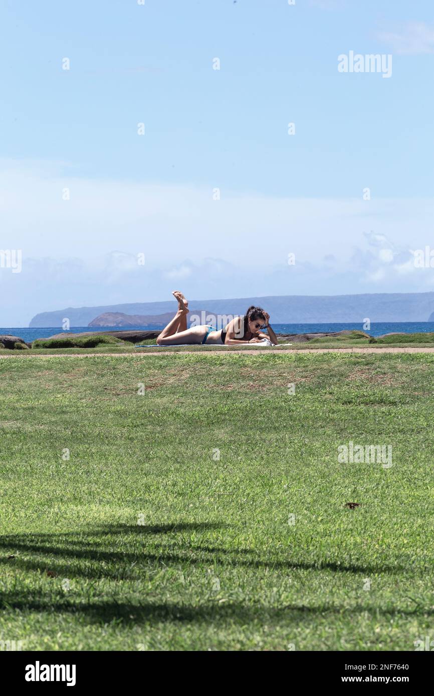 Frau, die sich hinlegte, während sie ein elektronisches Buch las. Sie liegt in einem Park am Strand. Hawaii Stockfoto