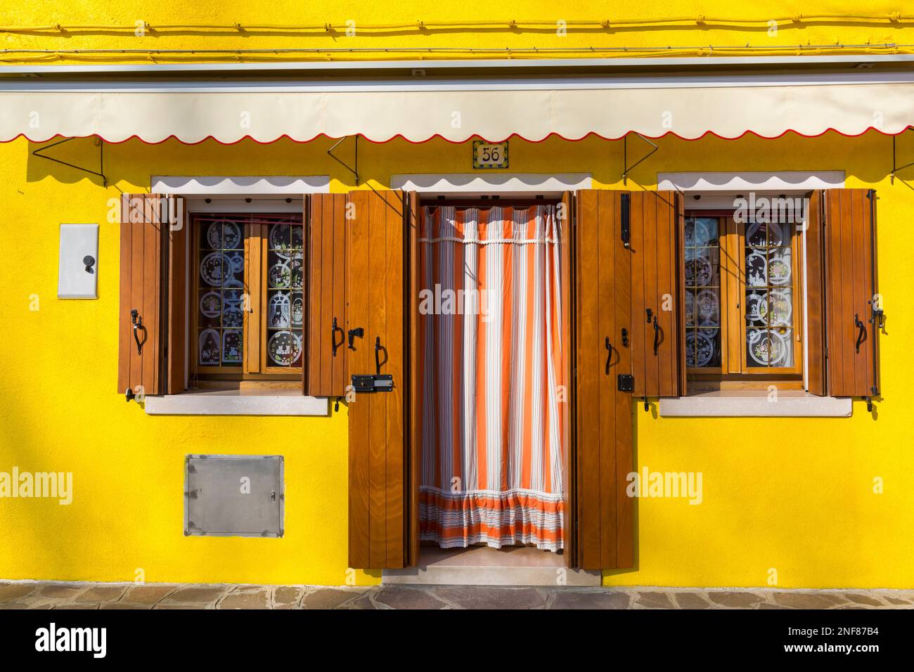 Eingang mit Vorhang und Fenster mit Fensterläden auf einem hellgelben Haus im Burano, Venedig, Italien im Februar Stockfoto