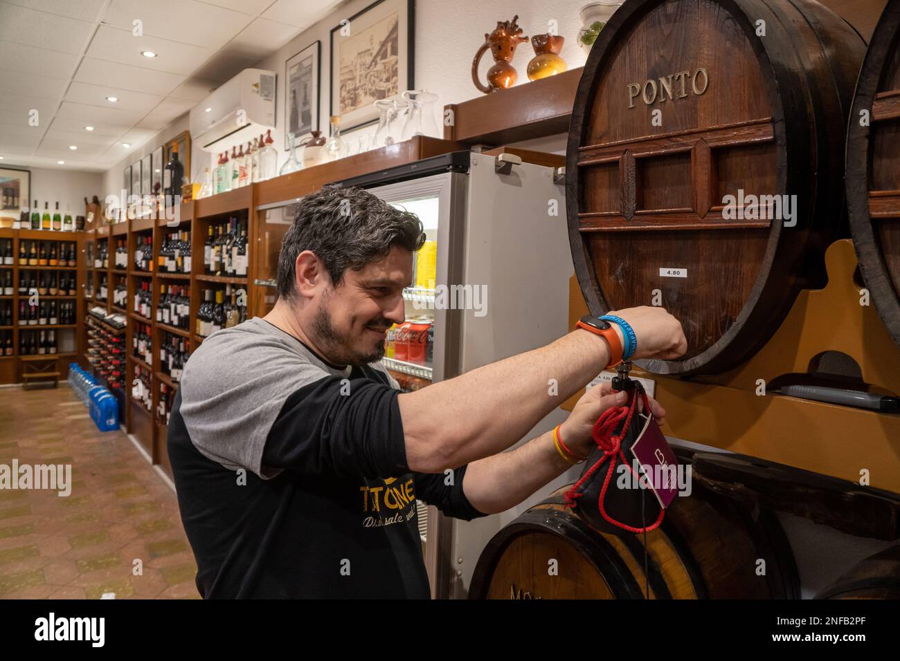 Fröhlicher Sommelier, der eine Lederweinchen aus einem Holzfass in einem luxuriösen Wein- und Spirituosenladen füllt Stockfoto