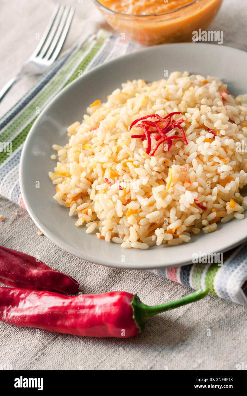 Würziger, parboilter Reis mit Karotten, gelben Zucchini und Chilischoten auf einem grauen Teller Stockfoto