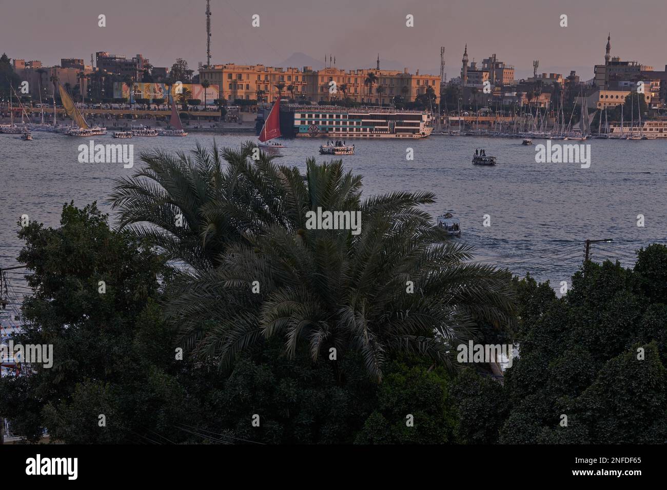 Luxor, Ägypten Sonnenuntergang vom Westufer aus, der den Nil mit Kreuzfahrtschiffen, Felukken und Winter Palace Hotel am Ostufer zeigt Stockfoto