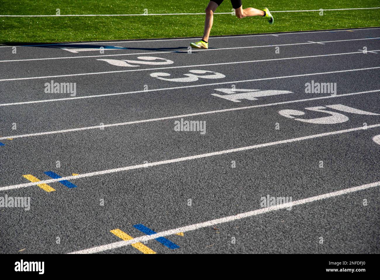 Ein Läufer auf einer grauen, sportlichen Laufstrecke mit großen weißen Zahlen. Läufer rast über Zahlen mit Platz zum Kopieren. Selektiver Fokus auf der Rennstrecke für hervorragende Ergebnisse Stockfoto