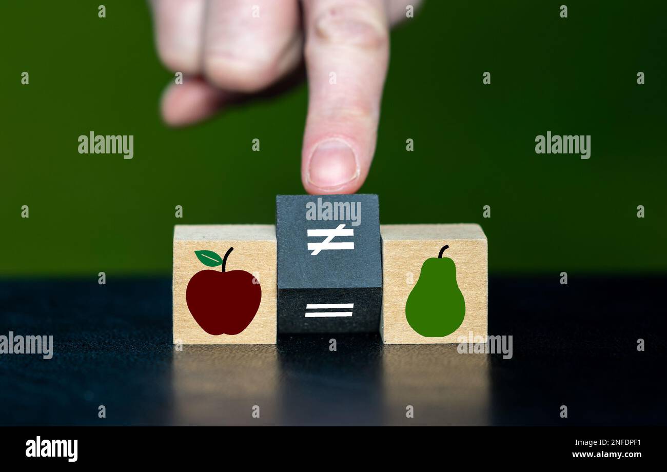 Symbol für den Satz, dass man Äpfel nicht mit Birnen vergleichen kann. Die Hand dreht den Holzwürfel und ändert das Gleichheitssymbol in ein ungleiches Symbol. Stockfoto