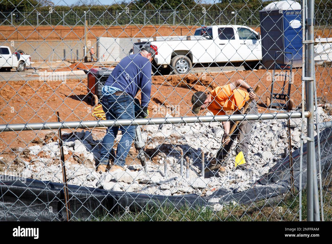 HICKORY, NC, USA – 14. FEBRUAR 2023: Zwei Bauarbeiter – einer mit Schaufel, einer mit Presslufthammer, hinter einem Kettengliederzaun. Stockfoto