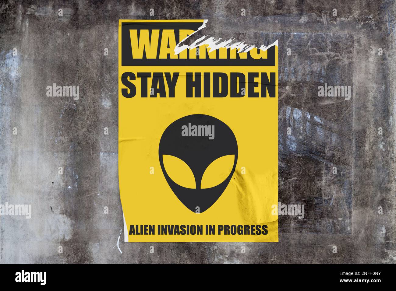 Durchgehende verwitterte Betonwand mit einem zerrissenen gelben Poster in der Mitte, auf dem ein Alien-Gesicht mit „Achtung: Versteckt bleiben, Alien-Invasion in PROG Stockfoto