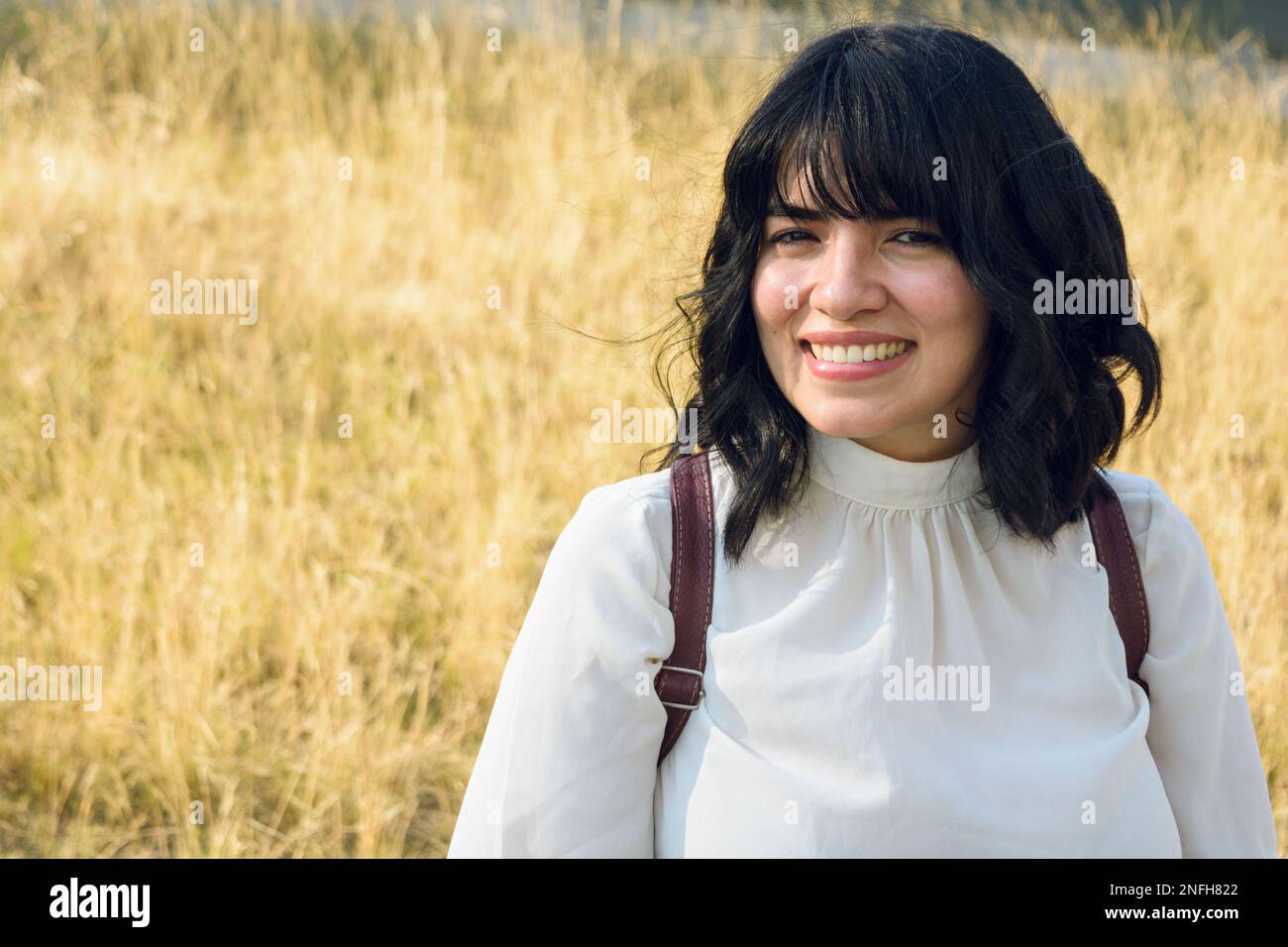 Porträt einer hellhäutigen Latina-Frau, die ruhig und glücklich draußen sitzt, lächelt und in die Kamera schaut Stockfoto