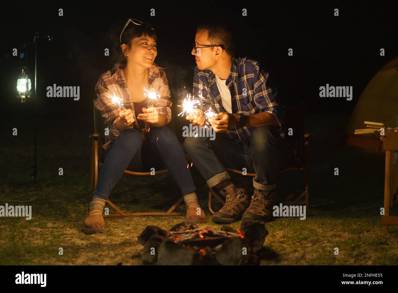 Ein asiatisches Paar zündet an einem Lagerfeuer ein funkelndes Feuer an, wo es nachts ein Zelt am See aufbaut. Stockfoto