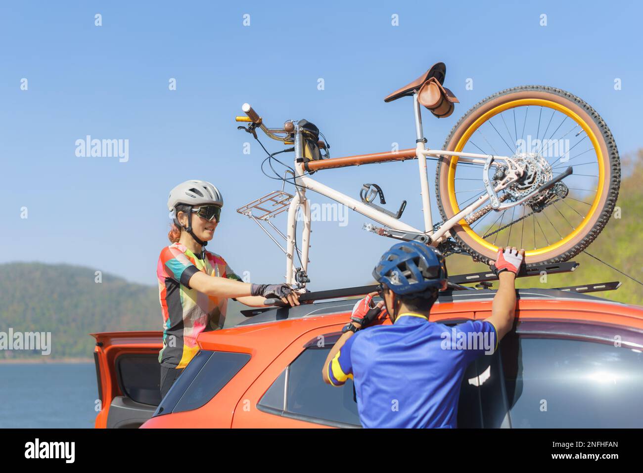 Asiatische Radfahrer laden ihre Fahrräder vom Dach ihres Autos ab, um sich auf eine morgendliche Radtour am See vorzubereiten. Stockfoto