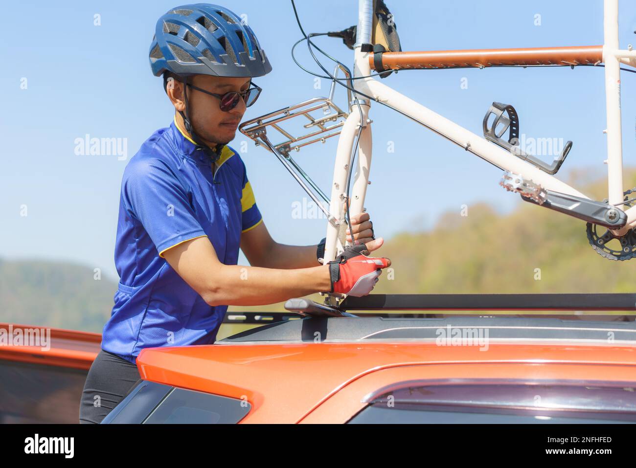 Asiatischer Fahrradfahrer, der auf dem Dach seines Autos einen Fahrradständer installiert, um sein Fahrrad nach der Fertigstellung seines Fahrrads aufzubewahren. Stockfoto