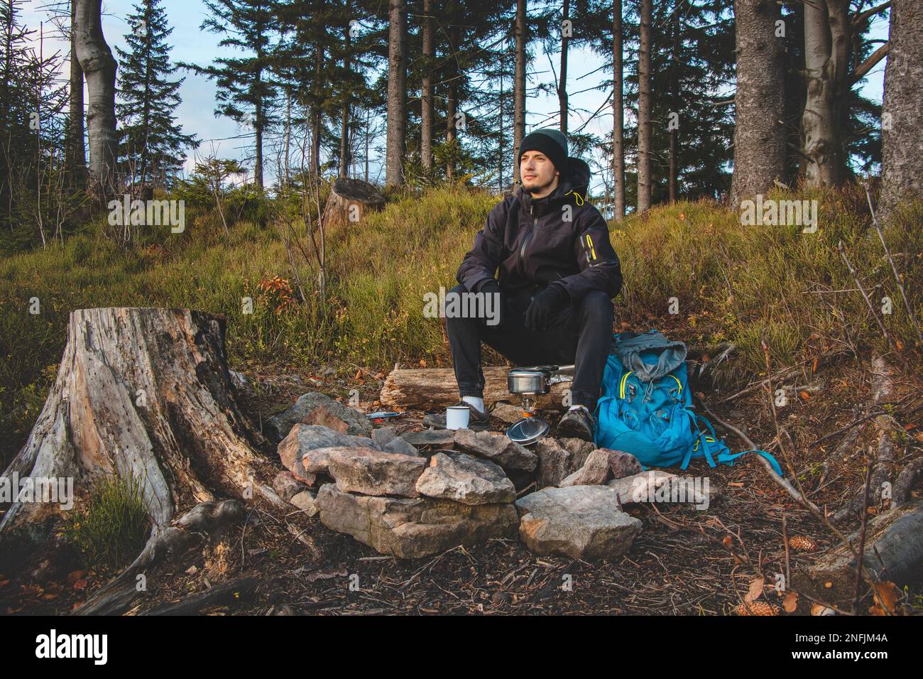 Wildnis-Trekking-Enthusiasten sitzen am Lagerfeuer und frühstücken bei Sonnenaufgang. Frühstück und Vitamin D auf dem Hügel zu fangen. T Stockfoto