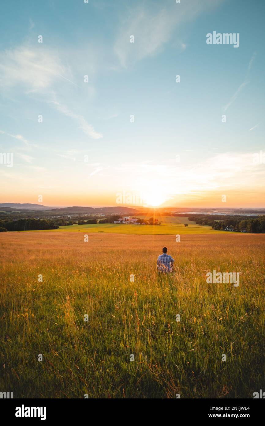 Ein Mann, der auf einem Maisfeld sitzt, denkt über seine Zukunft nach und blickt in den Sonnenuntergang. Selbsterziehung, Beherrschung von Achtsamkeit. Beskydy Mountains, Tschechische Republik. Stockfoto