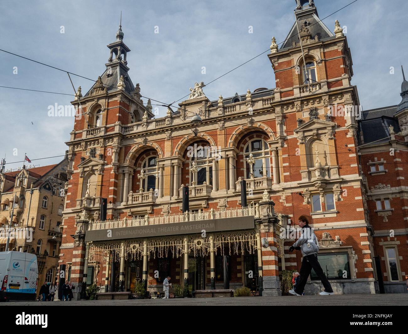 Blick auf das International Theater mit vorbeifahrenden Menschen. Amsterdam ist eine der schönsten, kreativsten und fahrradfreundlichsten Städte Europas. Es hat eine tolle Mischung aus kosmopolitischem Flair und eine relativ kleine Größe, was bedeutet, dass es einen Dorfcharme hat. Obwohl es immer noch kalt, aber sonnig ist, besuchen Touristen bereits die niederländische Hauptstadt an Wochentagen. Die am häufigsten besuchten Orte sind in der Regel der Dam-Platz, das Stadtzentrum und die Museen und Kanäle. Stockfoto