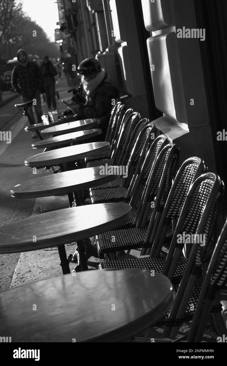 Monochrome Straßenszene mit Tischen und Stühlen vor Einem Café, bei der Eine Frau im französischen Frühling Paris Einen Kaffee Trinkt Stockfoto
