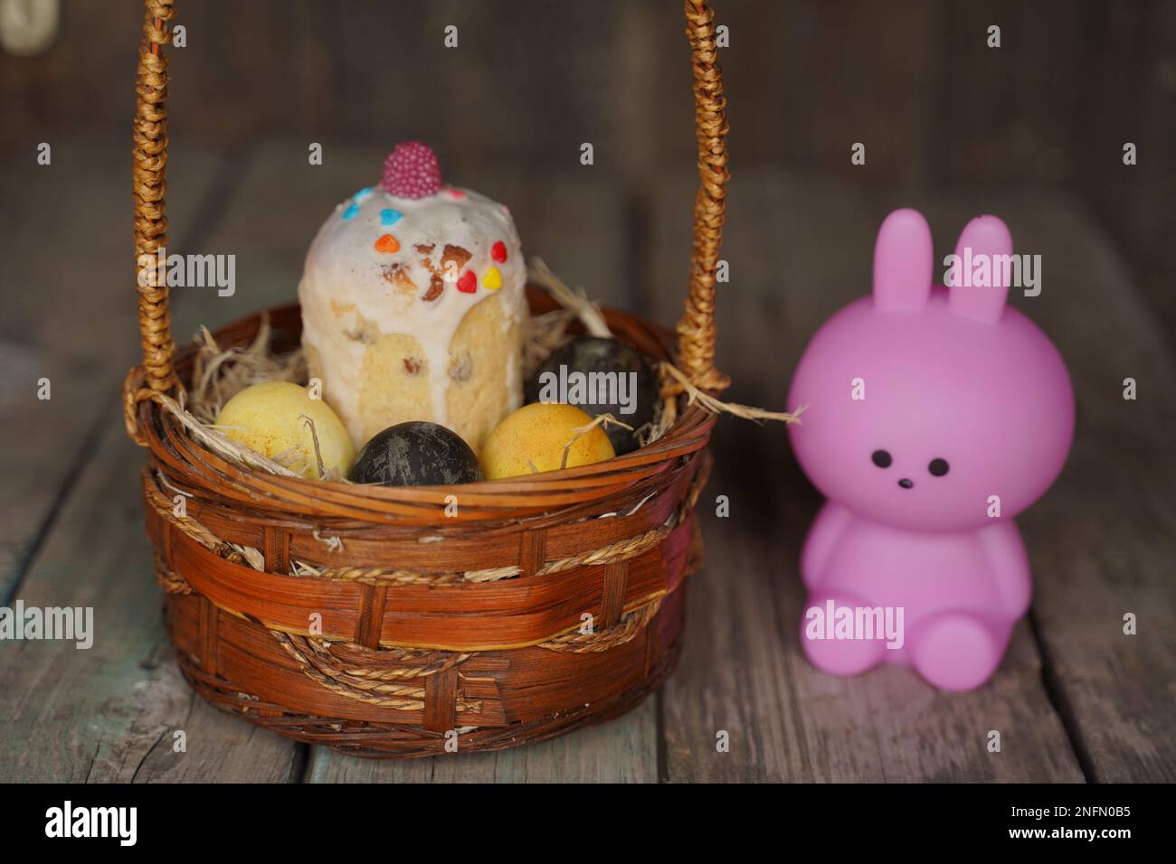 Hase oder Hase und bunte Esthers Eier im Korb. Süßes kleines rosa Kaninchen und Esthers Eier auf Holzhintergrund. Rabit steht Stockfoto
