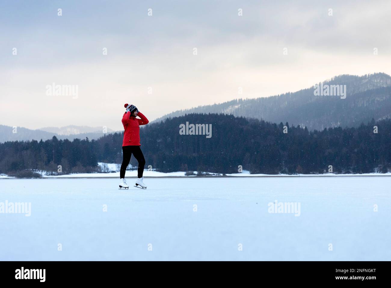 Frau in rotem Anorak Schlittschuhlaufen in der Natur auf einem wunderschönen natürlichen gefrorenen Cerknica-See, Slowenien Stockfoto
