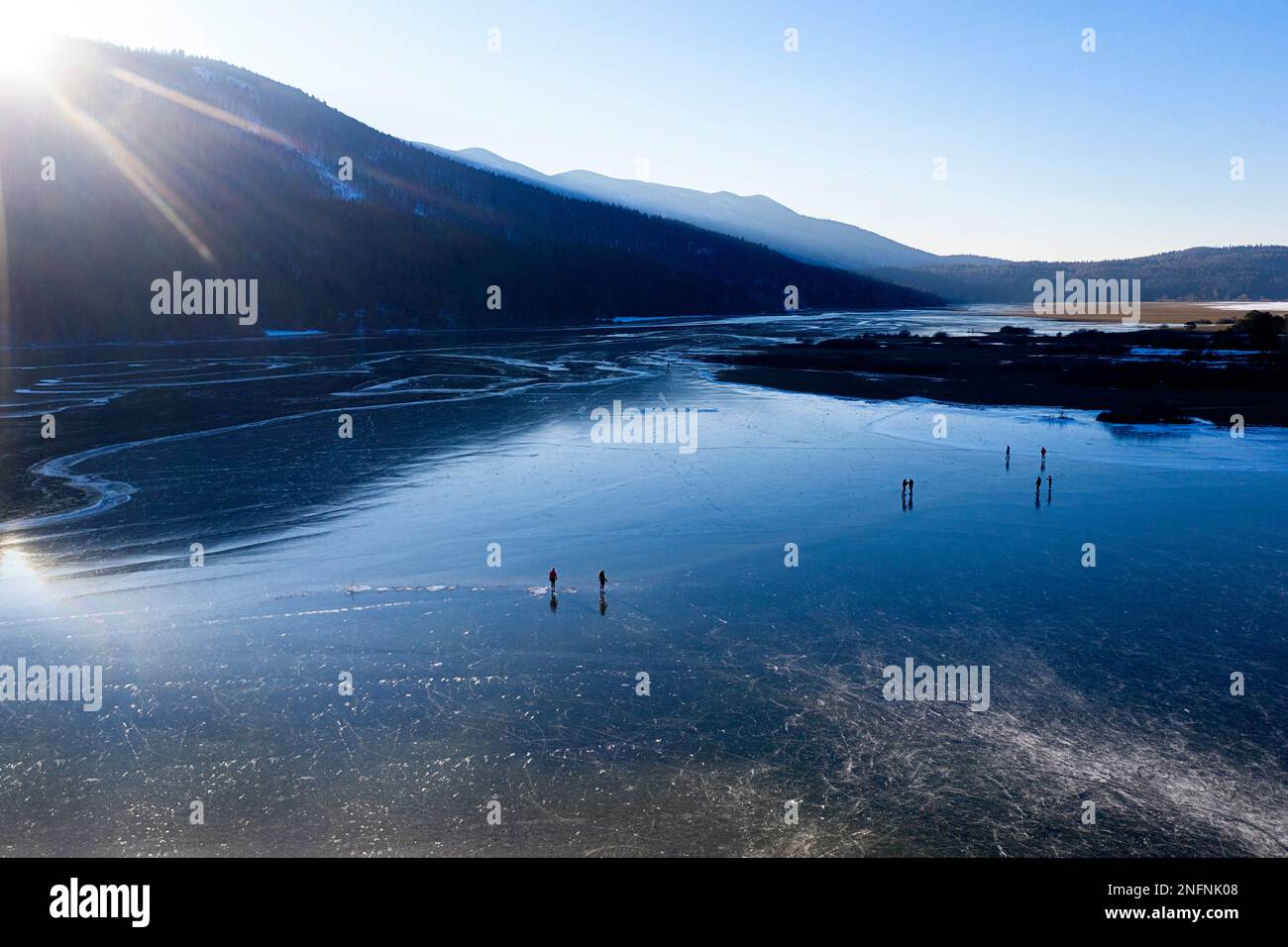 Die Menschen fahren am Ende eines sonnigen und kalten Wintertages in Slowenien Schlittschuhlaufen in der Natur auf einem wunderschönen natürlichen gefrorenen Cerknica-See Stockfoto