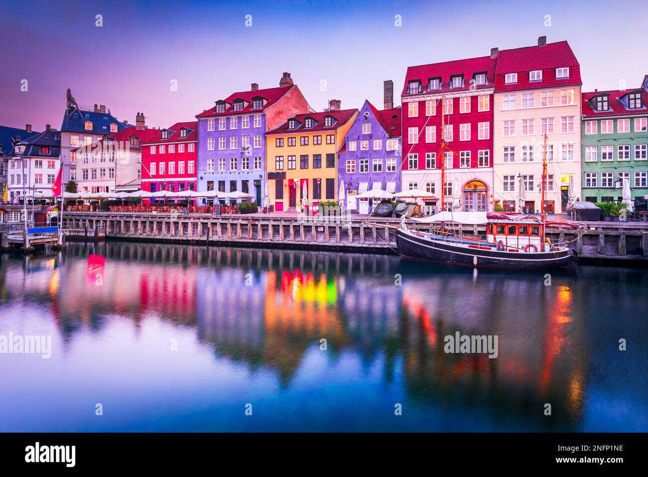 Kobenhavn, Dänemark. Nyhavn, Kopenhagens ikonischer Kanal, reflektiert farbenfrohe Gebäude und glühende Straßenlaternen in der Dämmerung, was zu einem malerischen Tourist wird Stockfoto