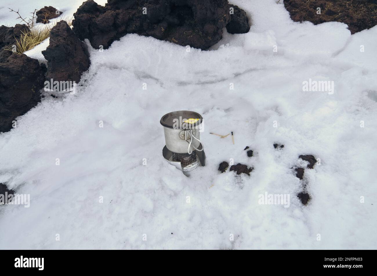 Metallbecher Rucksacktouristen mit Deckel auf sehr einfachem DIY-Alkohol-Herd und Windschutzscheibe auf dem Schnee des Ätna-Nationalparks, Sizilien, Italien Stockfoto