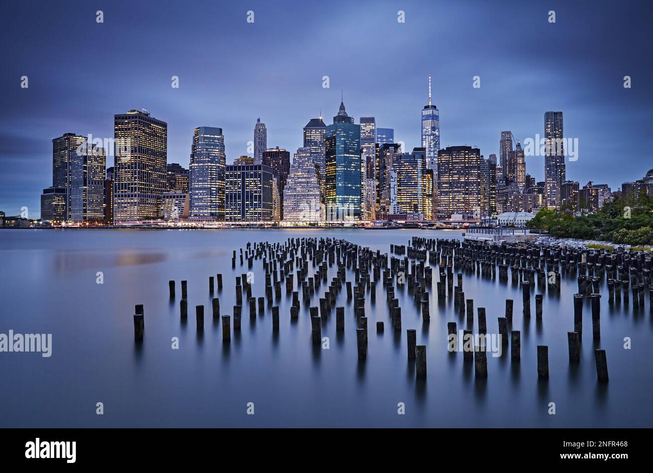 Holzstämme im East River und die Skyline von Lower Manhattan zur Blue Hour, Langzeitfoto von New York, Blick vom Brooklyn Bridge Park Stockfoto