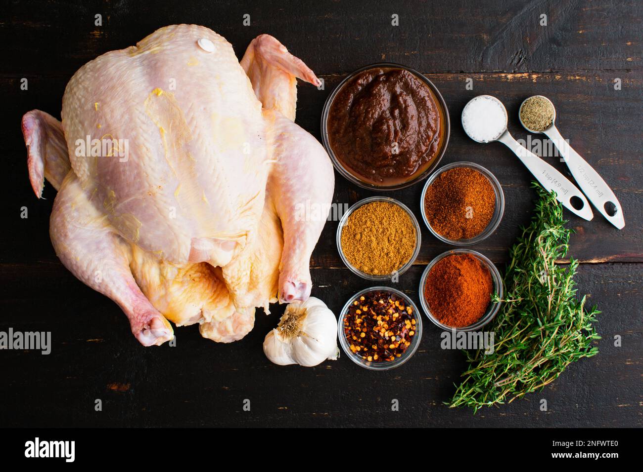 Apfelbutter geröstetes Hähnchen Zutaten auf einem Holztisch: Rohes Hähnchen, Apfelbutter und Gewürze auf dunklem Holzhintergrund Stockfoto