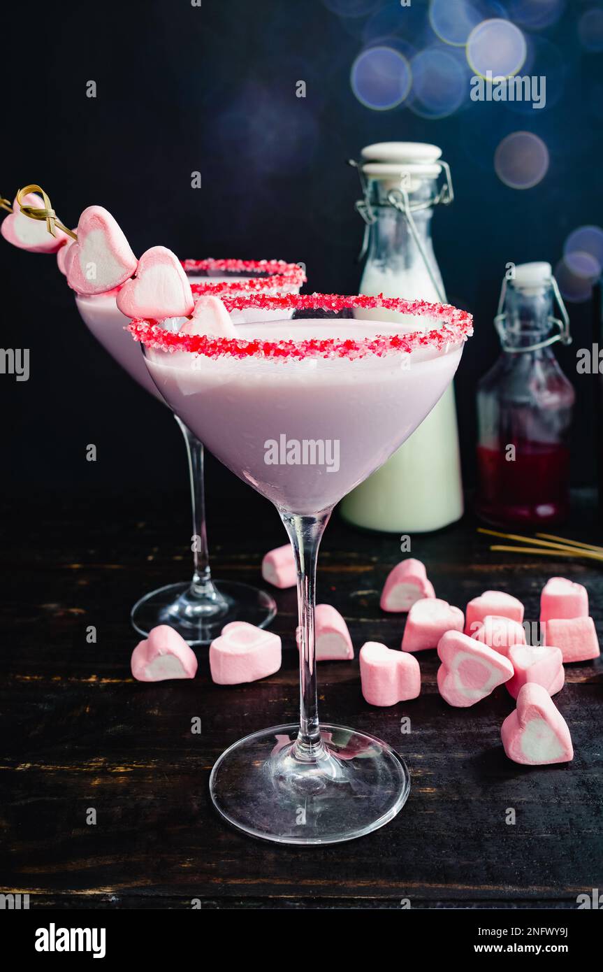 Valentinscocktail mit Himbeere und weißer Schokolade: Rosafarbener Cocktail in einem martini-Glas mit Streuseln und mit Herzmarshmallows garniert Stockfoto