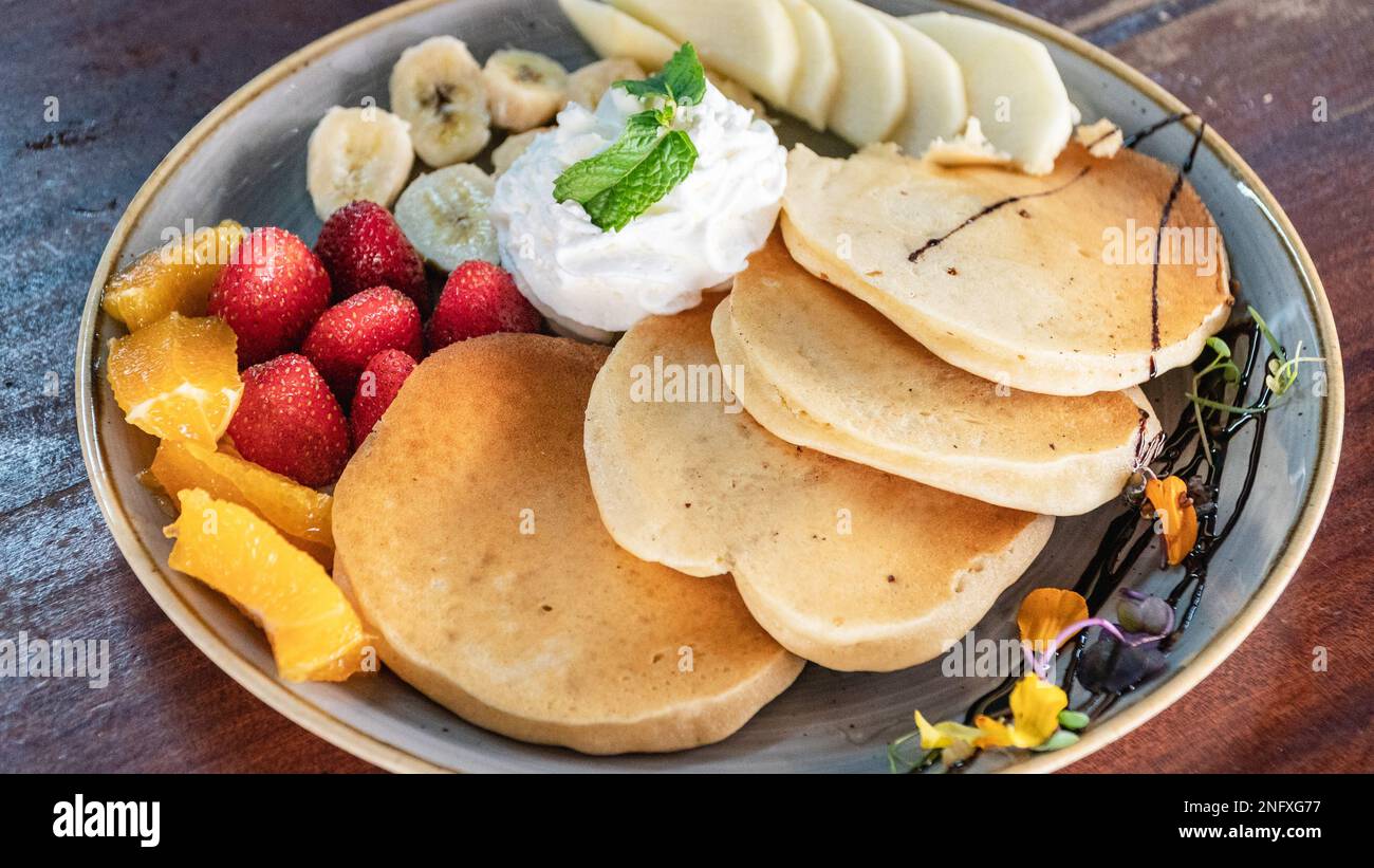 Ein Bild von frisch zubereiteten amerikanischen Pfannkuchen, abgetrennt mit frischem Obst und Sahnevögeln aus der Vogelperspektive Stockfoto