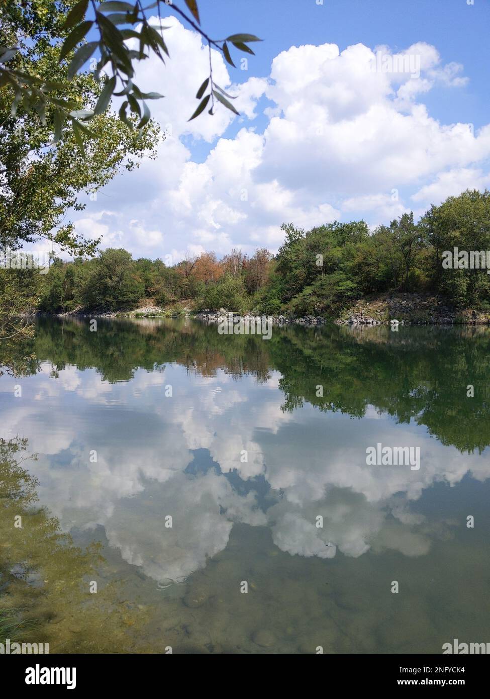 Die Reflexion von flauschigen Wolken auf einem wunderschönen Spiegelsee, umgeben von grüner Vegetation Stockfoto
