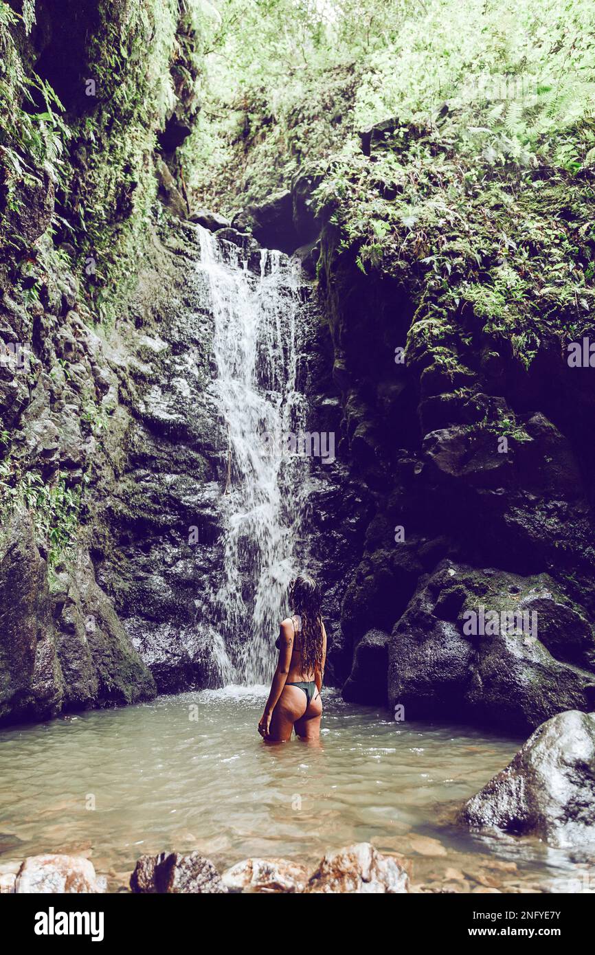 Junge Frau, die im Wasser steht und den Wasserfall beobachtet. Reisen und Abenteuer. Die Natur. Maui. Weg nach Hana Stockfoto