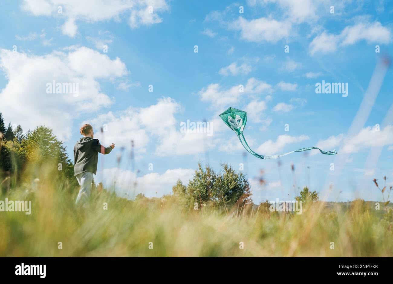 Ein Teenager auf der grünen Wiese wirft einen grünen Drachen mit einem langen Schwanz ab. Fröhliche Kindheitserlebnisse oder Konzeptfoto „Zeit im Freien verbringen“ Stockfoto