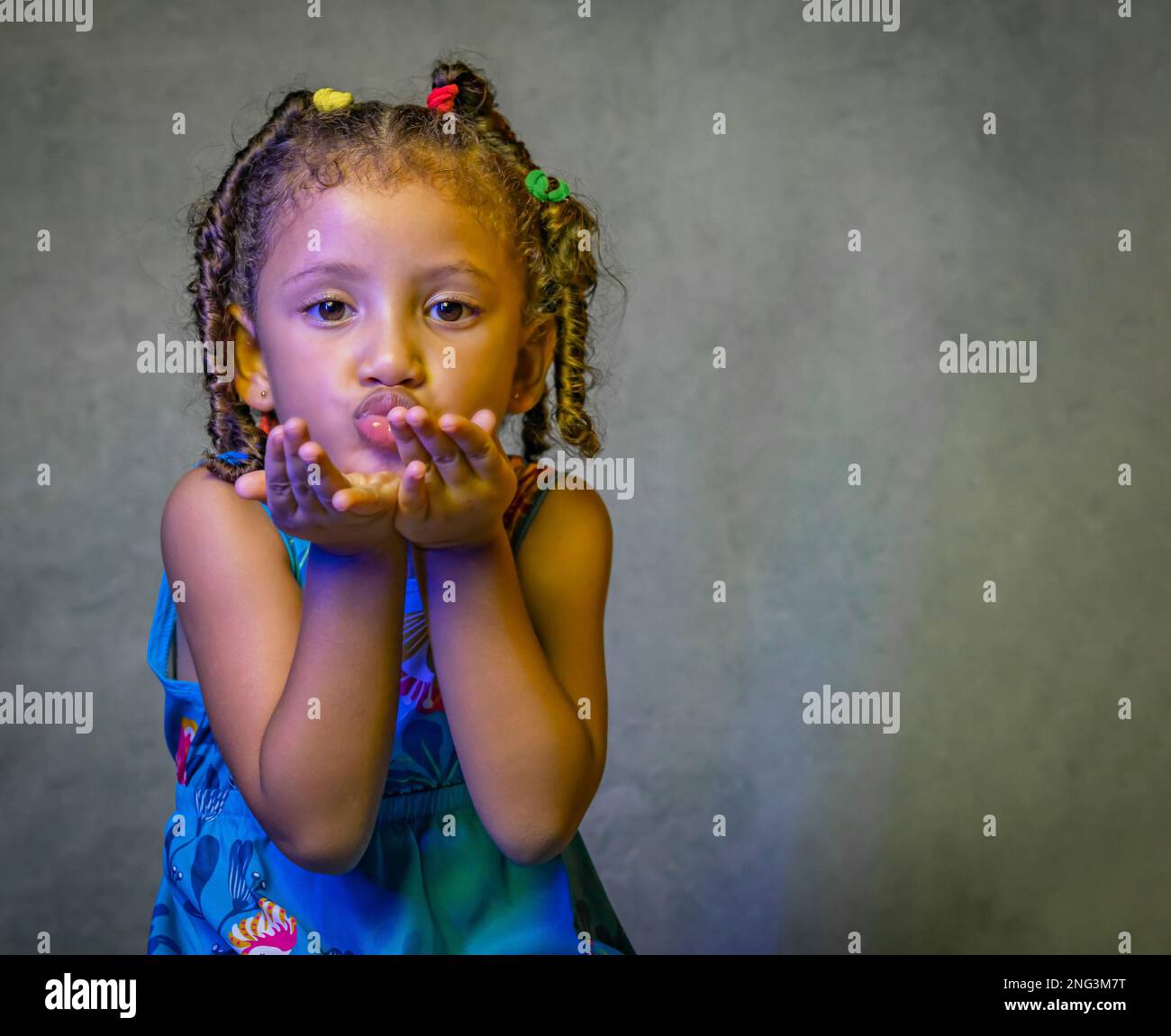 Studio-Porträt eines wunderschönen kleinen Mädchens in wunderschönem blauen Kleid auf lila Hintergrund, brasilianisches Mädchen lächelt, küsst und macht lustige Gesichter Stockfoto