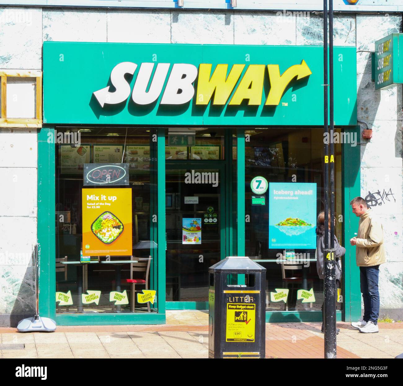 Zwei Personen stehen an sonnigen Sommertagen vor einem Subway Franchise Outlet Shop mit Subway-Schild im Stadtzentrum von Großbritannien. Stockfoto
