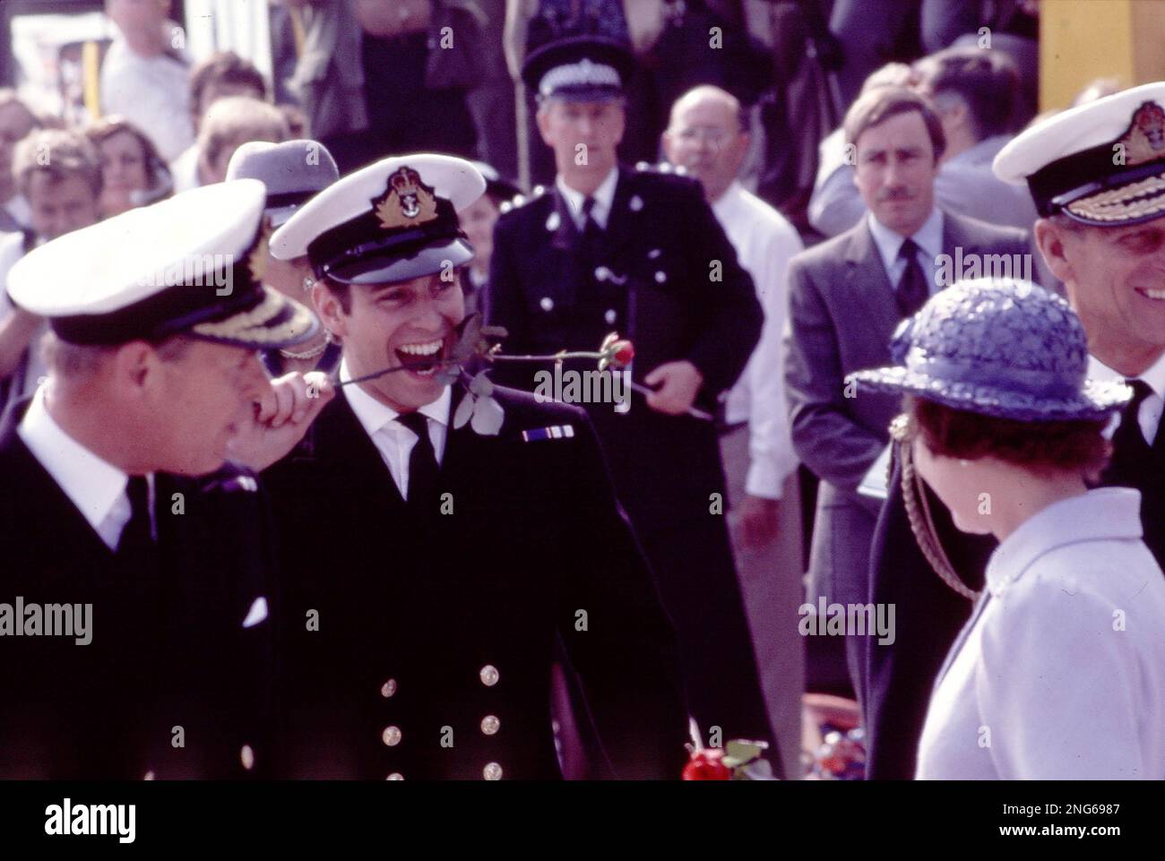 Britain's Prince Andrew bites the stem of a red rose after stepping ashore from the aircraft carrier HMS Invincible at Portsmouth Harbour, England, on Sept. 17, 1982. A red rose was presented to each member of the crew after returning from 166 days at sea. The 22-year-old prince is a helicopter pilot on the vessel. Queen Elizabeth II and Prince Philip, right, smile at their sons antics. (AP Photo/David Cauklin) Stockfoto