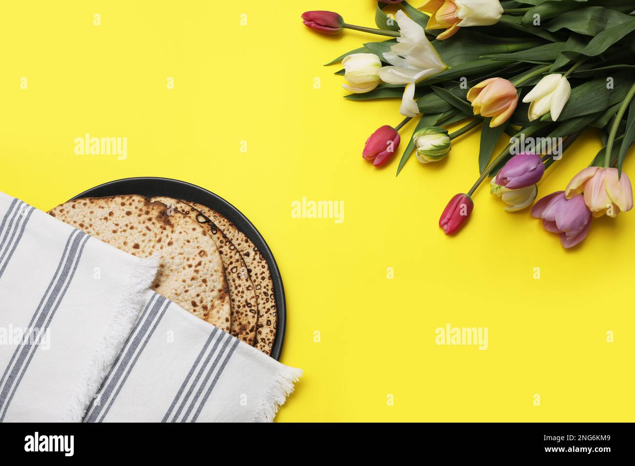 Leckere Matzen und frische Blumen auf gelbem Hintergrund, flach liegend. Pessach-Feier Stockfoto