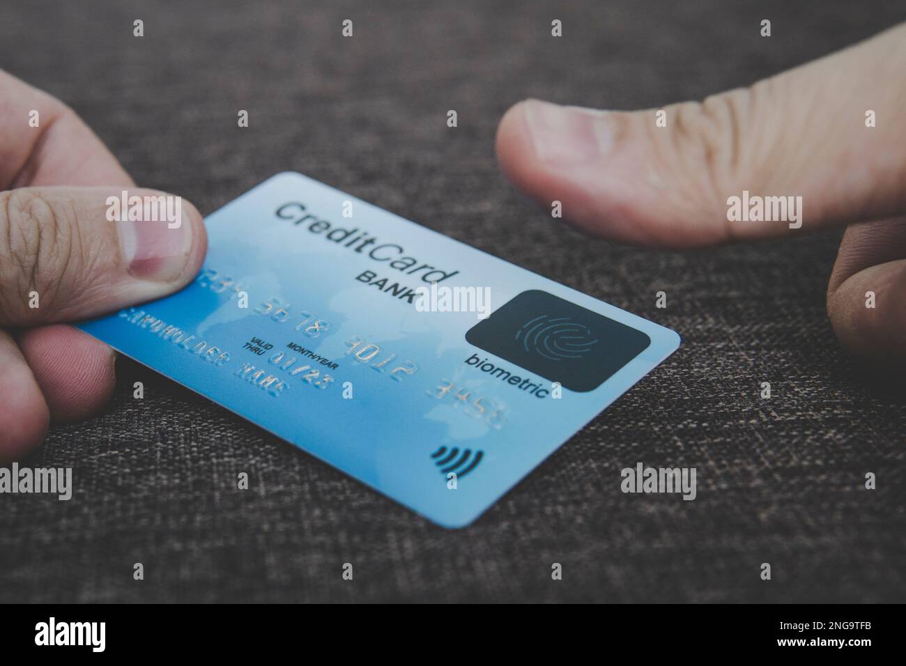 Nahaufnahme der männlichen Hände mit Kreditkarte mit Fingerabdruck-Scanner und Einbettung des Daumens, um online zu bezahlen. Konzept der Verwendung biometrischer Technologie in BA Stockfoto